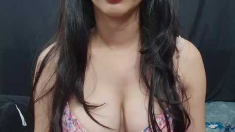 Media: A video of a woman with long, dark hair and light skin, wearing a low-cut, floral-patterned bra, standing against a black backdrop. Her cleavage is prominent.