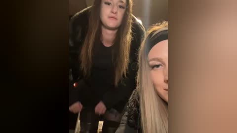 Media: Video of two women, one with long brown hair, black top, and holding drumsticks, and another with blonde hair, black headband, and makeup, both smiling.