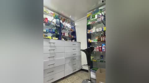 Media: Video of a well-lit, organized pharmacy with white cabinets, glass shelves stocked with various medicines, and a black scale in the foreground.