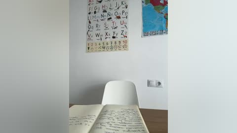 Media: Video of a minimalist classroom corner featuring a white chair, open book, and a wall adorned with educational posters, including a colorful world map.