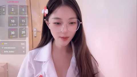 Media: Video of an Asian woman with long black hair, wearing clear-framed glasses, a white lab coat, and a pink flower hairpin. Background includes a temperature chart and wooden door.