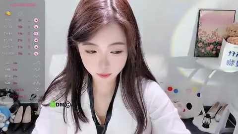 Media: A video of an East Asian woman with long black hair and fair skin, wearing a white lab coat, sitting at a desk with a calendar and colorful markers in the background.