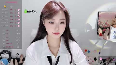 Media: Video of a young East Asian woman with long, straight brown hair, wearing a white shirt and black tie, standing in a bright, modern room with a TV displaying a landscape painting.