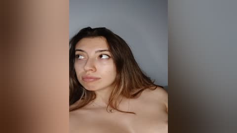 Media: Video of a young woman with light brown skin, long brown hair, and dark eyes, gazing thoughtfully into the distance, partially obscured by a beige curtain.