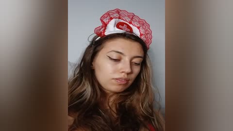 Media: A video of a young woman with long, wavy brown hair wearing a red lace nurse cap, looking downward with a serene expression.