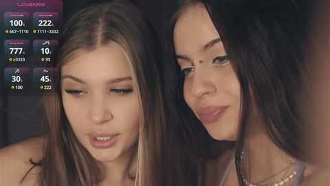 Media: Video of two young women with long hair, one with light brown, the other with dark brown, engaged in conversation. Background is blurred, with a digital display showing social media metrics in the top left corner.