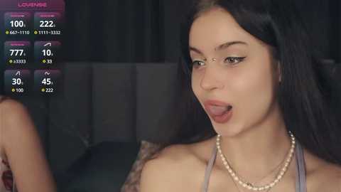 Media: A video of a young woman with fair skin, dark hair, and a pearl necklace, sticking out her tongue. The background shows a dark room with a gray couch.