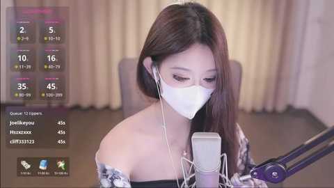 Media: Video of an Asian woman with long brown hair, wearing a white mask and headphones, singing into a microphone in a dimly lit room with beige curtains.