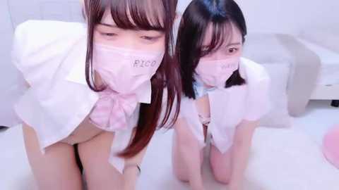 Media: Video of two young Asian women in maid costumes with pink masks and white aprons, kneeling on a white floor in a minimalist room.