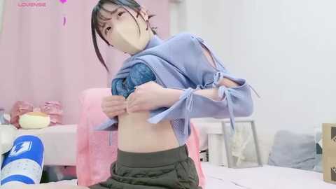 Media: Video of an Asian woman with short black hair, wearing a blue and white striped top, pulling it over her head, revealing her bare midriff, in a pink and white bedroom with stuffed toys and a bed.