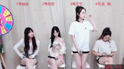 Media: Video of four East Asian women in casual clothing, sitting against a white backdrop, with a colorful pinwheel in the background.