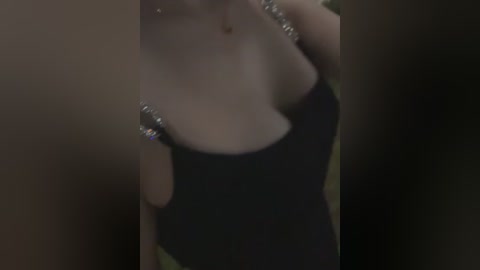 Media: Video of a woman wearing a black, low-cut, sleeveless dress adorned with silver sequins. Her fair skin and slender physique are partially visible, with a blurred background suggesting an indoor setting.