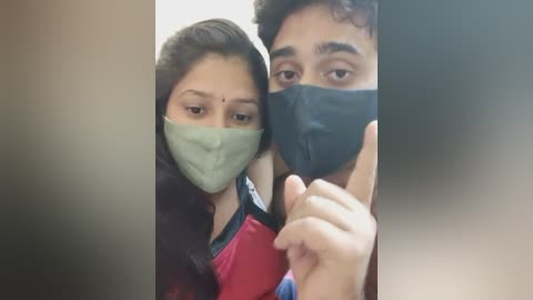 Media: A video of a young South Asian couple with light brown skin, wearing green and black face masks, holding hands. The woman has a bindi on her forehead.