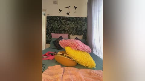 Media: A video of a cozy bedroom with a green bedspread, pink and yellow pillows, and a vibrant yellow blanket, featuring a leaf-patterned wall and bird silhouette decor.