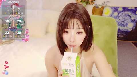 Media: A video of an Asian woman with straight brown hair, wearing a tank top, drinking from a milk carton, in a room with a green chair and a Van Gogh painting.