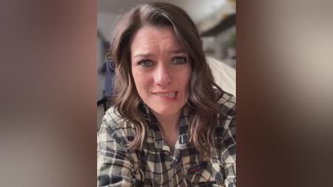 Media: Video of a woman with light skin and shoulder-length, wavy brown hair, wearing a plaid shirt, looking worried with a grimace.