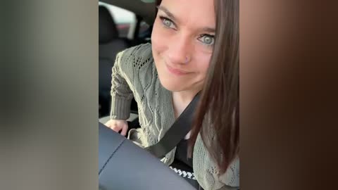 Media: Video of a smiling young woman with straight brown hair and green eyes, wearing a knitted green cardigan, driving in a car.