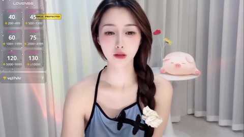 Media: Video of an Asian woman with fair skin, brown hair in a braid, wearing a blue apron, standing in a modern kitchen with white curtains and a pink piggy bank.