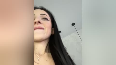 Media: A video of a smiling young woman with long black hair, wearing a cross necklace, standing in a plain room with white walls and a tall, modern lamp.