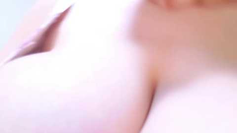 Media: A close-up video of a woman's bare chest with large, round breasts and pale skin, blurred background, soft lighting.