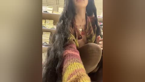 Media: A video captures a woman with long, dark hair, wearing a colorful, patterned sweater, seated in an office with shelves of yellow folders in the background.