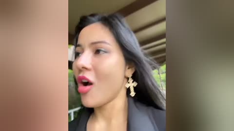 Media: Video of a woman with long dark hair, wearing bold red lipstick and large gold cross earrings, caught in a moment of surprise or excitement.