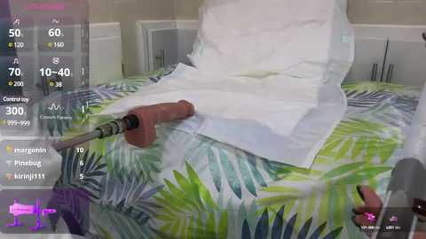 Media: Video of a person using a pink drill to puncture a white sheet over a green and blue patterned bedspread, with digital overlays displaying statistics.