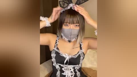 Media: Video of a woman with short, straight brown hair in a black lace bunny costume with a white frilled mask, adjusting her headband.