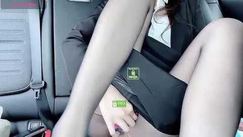 Media: Video of a woman in a black suit, bent over in a car, wearing sheer black stockings, with a green sticker on her thigh.