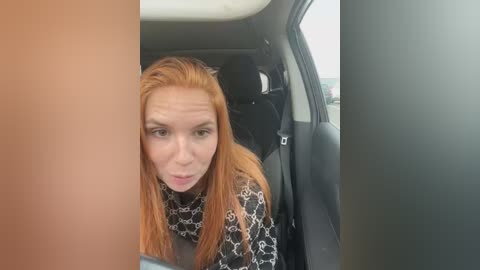 Media: A video of a Caucasian woman with long, straight red hair, wearing a black and white patterned top, making a funny face while sitting in a car.