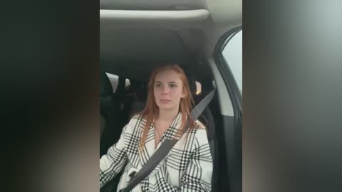 Media: Video of a young woman with light skin and long, straight, reddish-brown hair, wearing a white and black plaid shirt, seated in a car with a gray seatbelt across her chest.