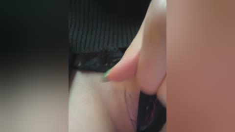 Media: A close-up video of a woman's hand with green-painted nails gently pulling apart black lace panties, revealing her shaved vulva. The background is blurred, focusing on the intimate action.