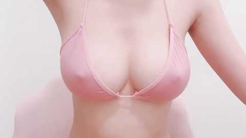 Media: Video of a fair-skinned woman's upper torso in a light pink halter top, revealing cleavage and smooth skin. Background is plain white, no visible accessories or additional objects.