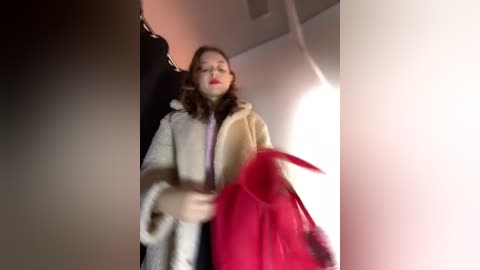 Media: A blurred video shows a woman in a beige coat and red handbag, smiling with closed eyes, in a dimly lit room with a white ceiling.