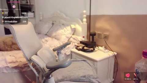 Media: Video of a messy bedroom with a white chair, unmade bed, and scattered clothes. A desk lamp and cables are on the right.