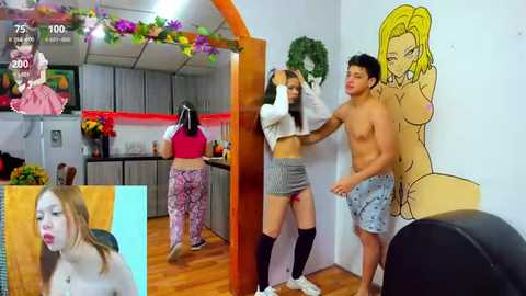 Media: Video of a young woman in a pink top and gray shorts, being held by two shirtless men in a kitchen with cartoon murals.