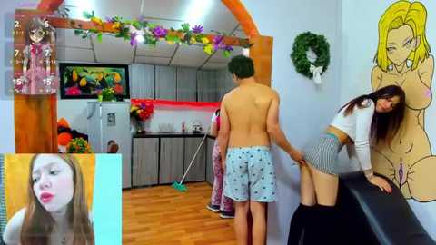 Media: Video of a young man with green hair, shirtless, wearing blue shorts, being held by a topless woman in a kitchen with festive decorations.