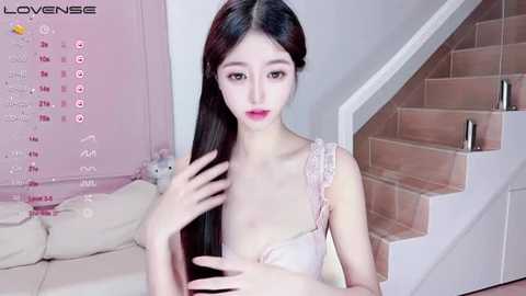 Media: Video of a slender East Asian woman with long black hair, wearing a light pink lace bra, standing in a pink-themed room with a white staircase and calendar.