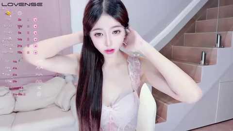 Media: A video of an Asian woman with long, straight black hair and fair skin, wearing a light pink lace bra, posing in a modern, softly lit bedroom with a staircase in the background.