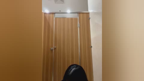 Media: Video of a modern, beige-tiled bathroom with a wooden-framed, beige-tiled shower stall and a black showerhead, featuring a minimalist design and recessed lighting.