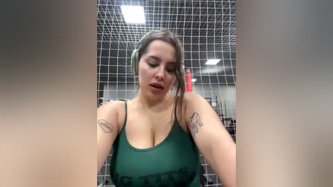 Media: A video of a plus-sized woman with medium skin tone, wearing a green tank top and headband, standing in a tiled shower with visible tattoos.