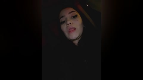 Media: Video of a young woman with fair skin, wearing dark makeup, sitting in a dimly lit car. Her expression is neutral, and she has a slight smile.