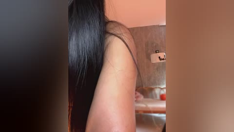 Media: Video of a woman with long, straight black hair, showing her side profile, in a dimly lit room with a beige wall and a modern lamp.