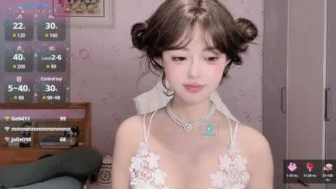 Media: Video of a young Asian woman with fair skin, dark hair styled in buns, wearing a lace white dress with floral detailing, and a silver choker, in a bedroom with a pink floral wallpaper, displaying live-streaming video metrics.