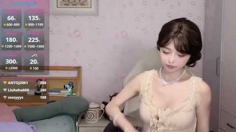 Media: A video of a slender Asian woman with short black hair, wearing a beige lace dress, sitting on a green couch in a room with light pink floral wallpaper.