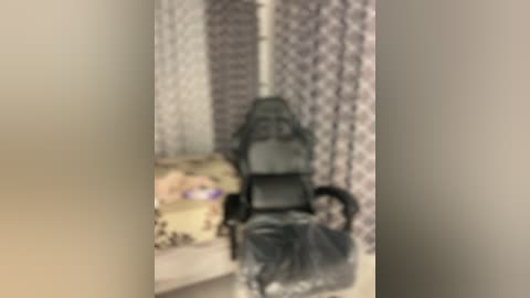 Media: Blurry video of a dark-skinned woman with a black hijab, sitting on a patterned couch. She holds a black bag. The background features a wall with intricate floral designs.