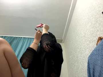 Media: Video of a woman applying makeup in a bathroom; she's holding a pink brush against a white wall with a teal curtain in the background.