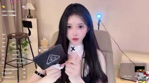 Media: A video of an East Asian woman with long black hair, wearing a white dress and black choker, sitting in a modern living room, holding a black book, with digital overlays showing live stream stats.