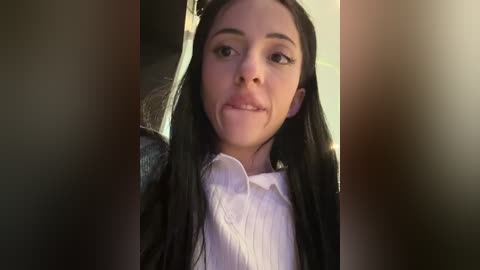 Media: A video of a young woman with long black hair and fair skin, wearing a white blouse, captured in a selfie-style, slightly out of focus.