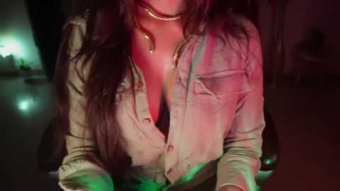 Media: A video of a woman with long, dark hair, wearing a low-cut, open denim shirt revealing cleavage, in a dimly lit room with green and red lighting.